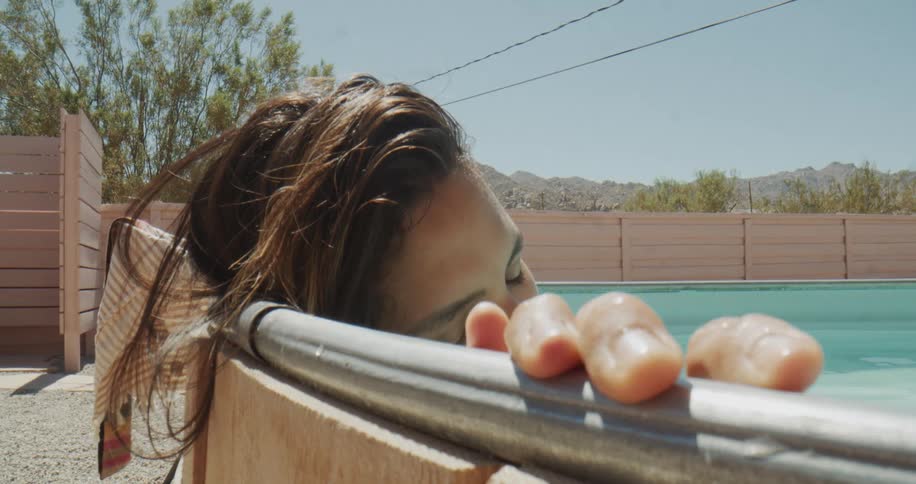 A woman sleeps inside a pool with her head and hand resting on the edge