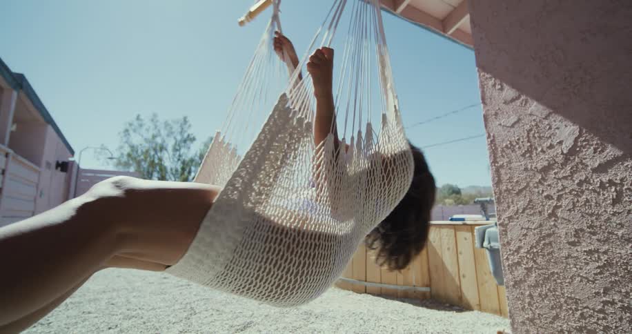 Woman swings in hammock chair near sandy yard with wooden walled pool