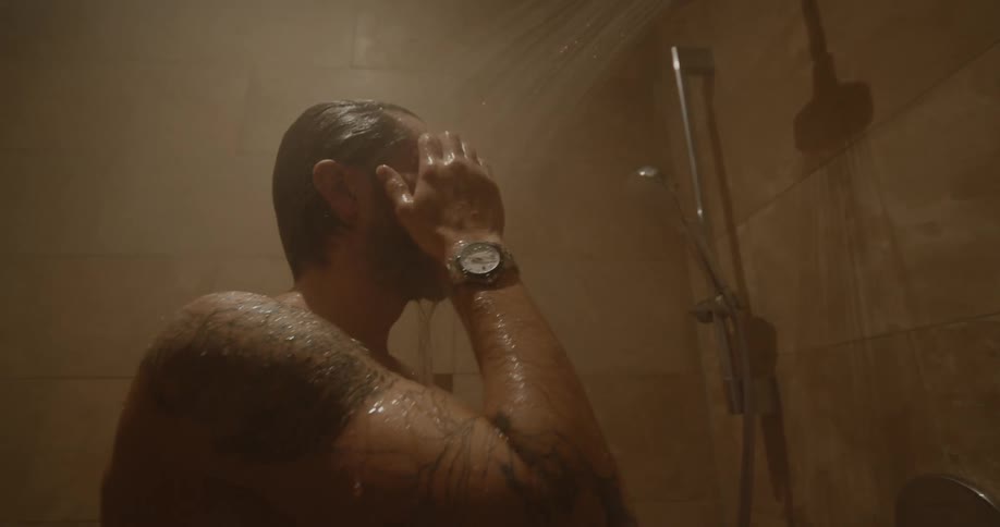 A man with tattoos on his arm and shoulder takes a steaming hot shower