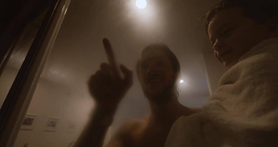 A father holds his son and traces his finger on the window