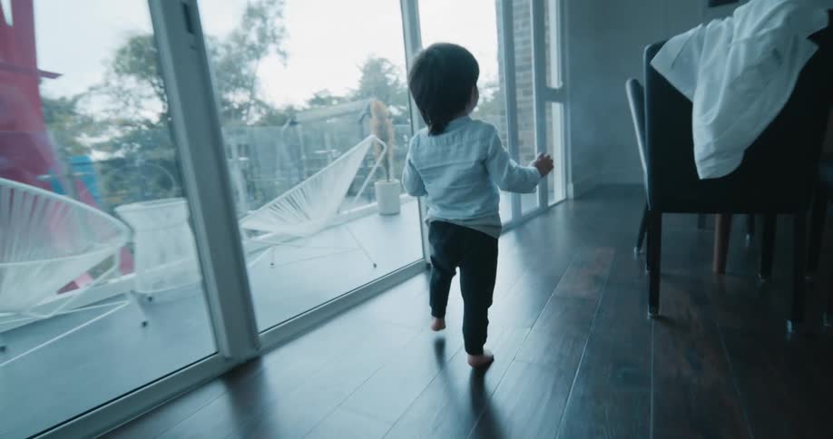 Young boy happily running around inside the house next to a glass door of a balcony