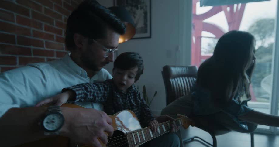 A man teaches his toddler son how to play guitar