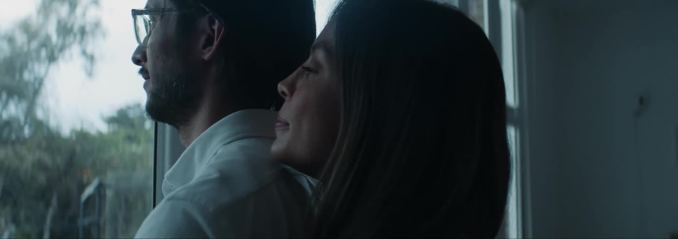 Woman hugging her husband from behind while they look outside through the window