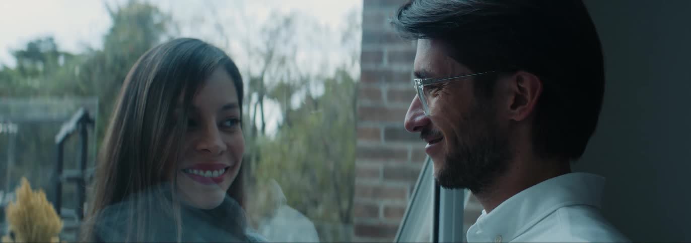 Man and woman standing in opposite sides of a glass window smiling and looking at each other in a romantic way