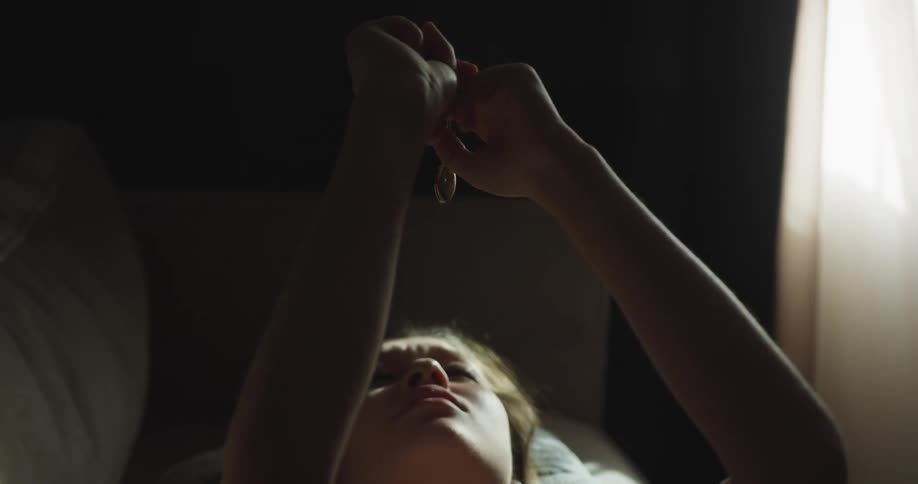 A woman lays on a couch with her arms above her head grasping a pendant