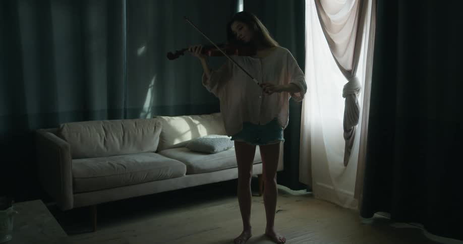 Young woman standing in the middle of an empty room and playing violin