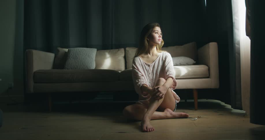 Young woman sitting in the floor in front of a couch looking outside through the window