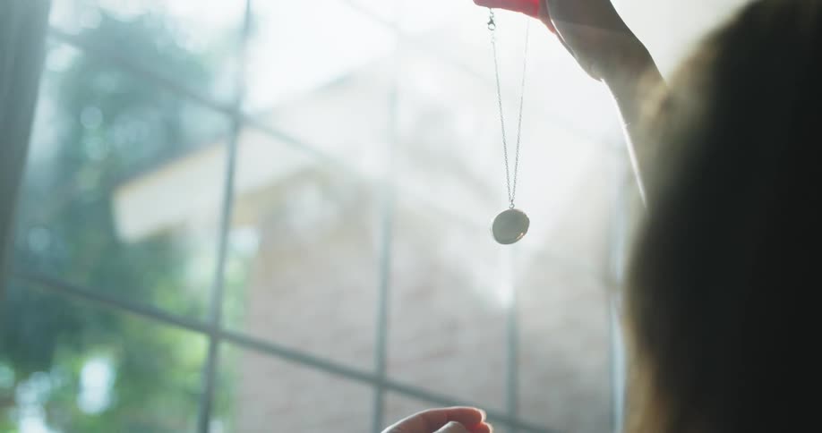 Woman holding up a necklace against the sunlight coming through window
