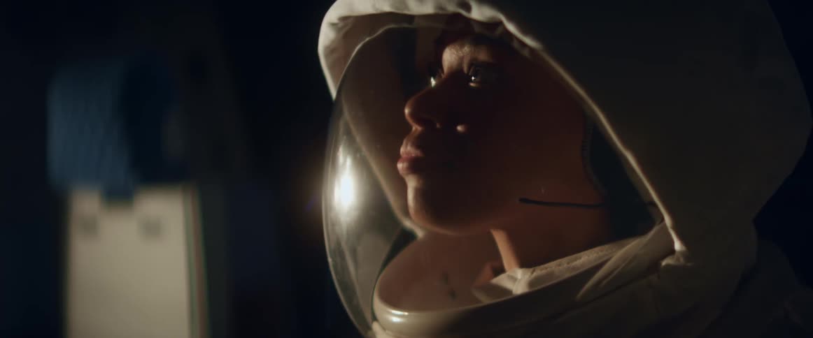 Black woman wearing a spacesuit shakes her head as she talks into a microphone