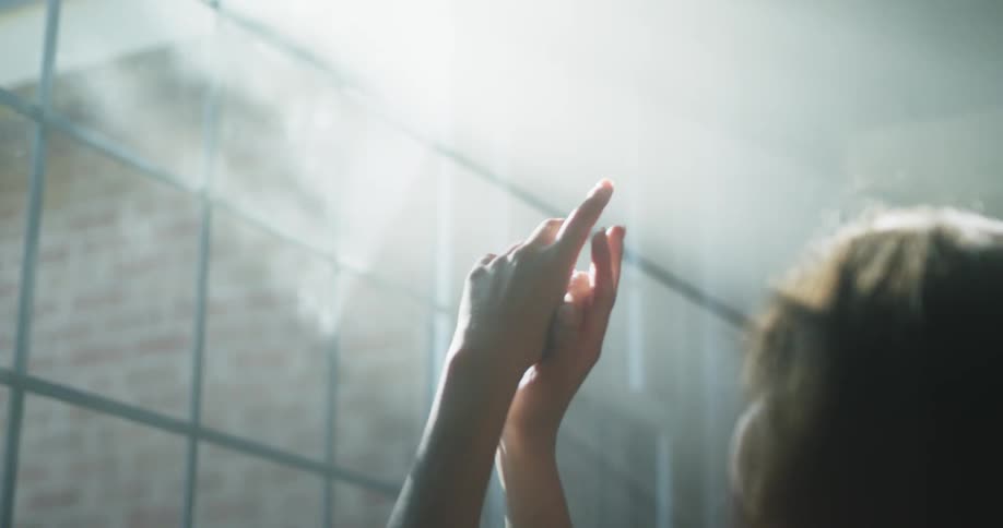Woman examines hands sitting in sun rays coming through window