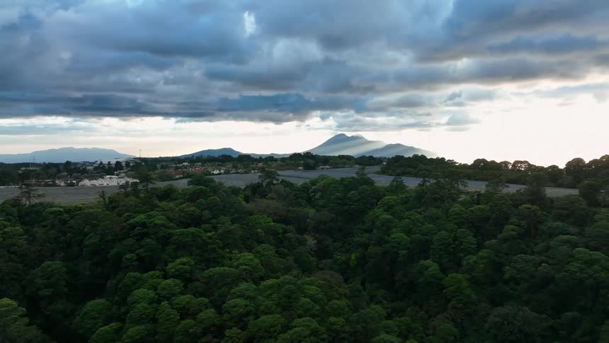 Dense clouds hover in the sky above a thickly forested area with a river running through it