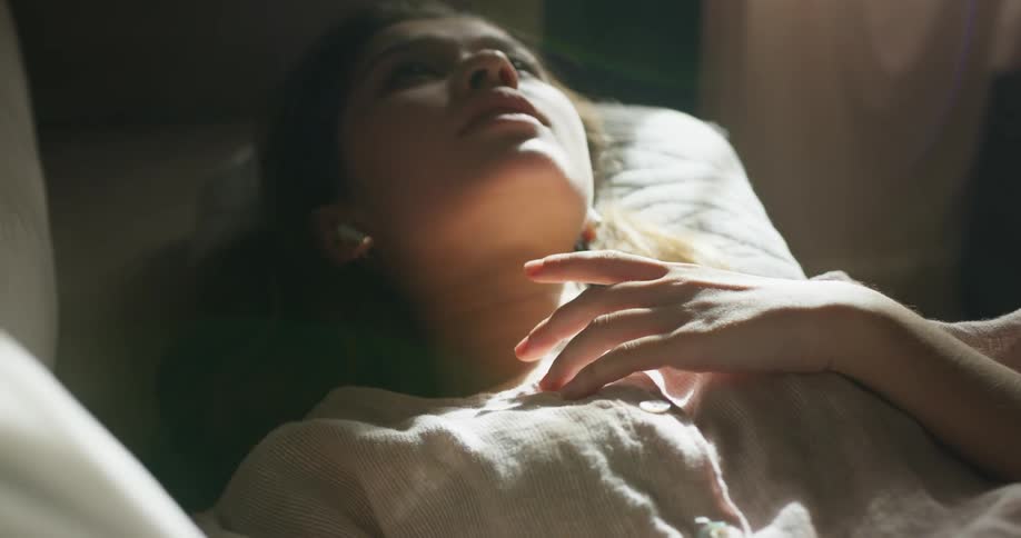 Teenage girl with white shirt wireless earphones lies on bed listening to music in bedroom