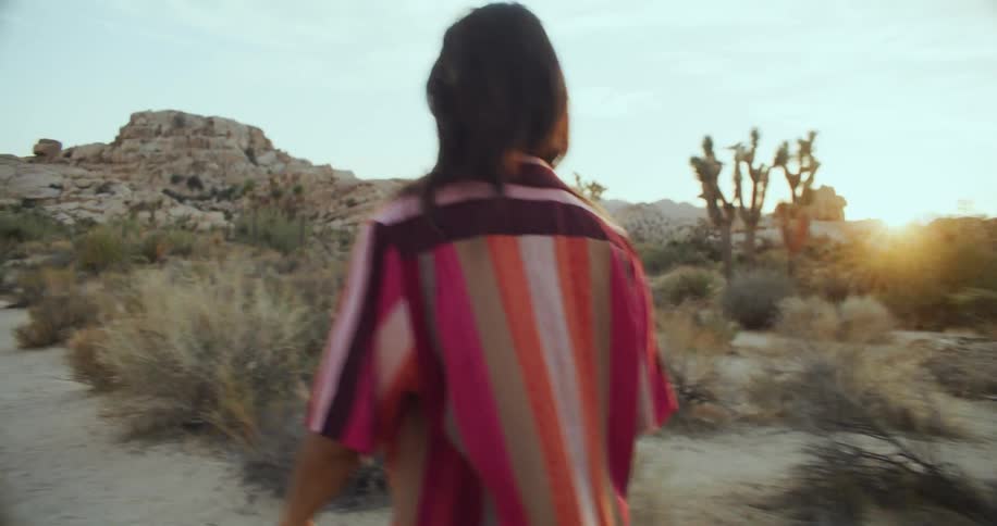 A woman walking across the landscape pushes her hair out of her eyes