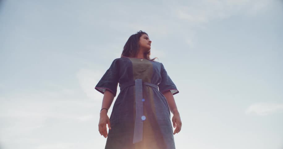 Woman in a blue dress and wearing a wristband stands under a blue sky