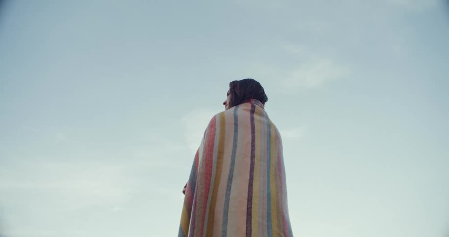 Woman standing outdoors wrapped in a colorful blanket at a sunny day