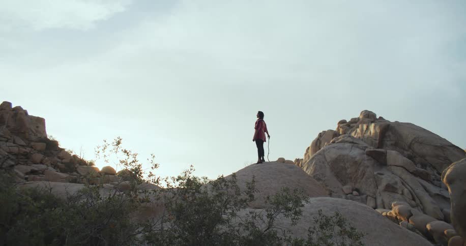 A woman stands atop a rock formation in the wilderness while holding a stick