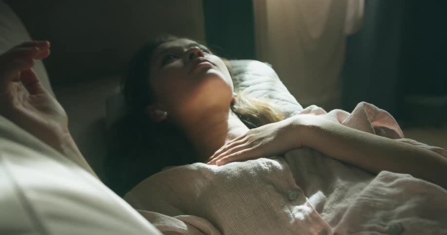 Young white woman lying down in a bed next to a window with sunlight coming in