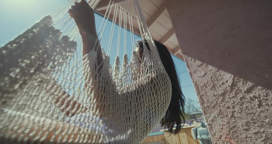 Latin woman sitting and swinging in a hammock in her backyard at a sunny day