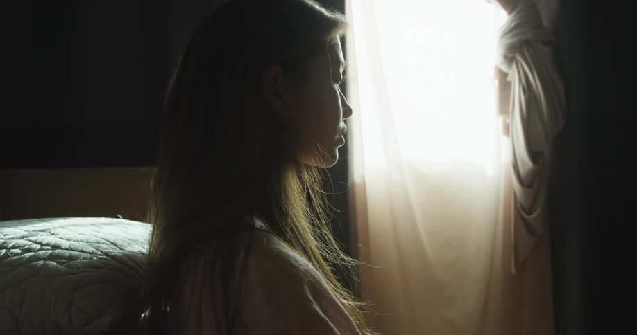 Young woman looks sad as she looks down while sitting in a bedroom