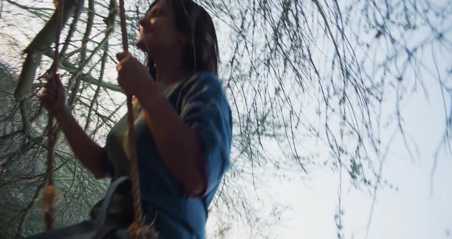 Latin woman swinging in the tree swing outdoors during sunset