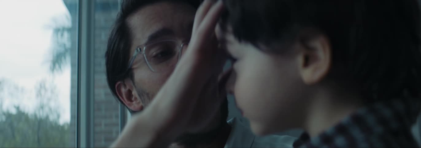 Father with glasses and beard holds son and looks out the windows
