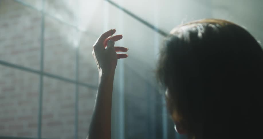 Woman holds a necklace up to the window and examines it under the bright sunlight