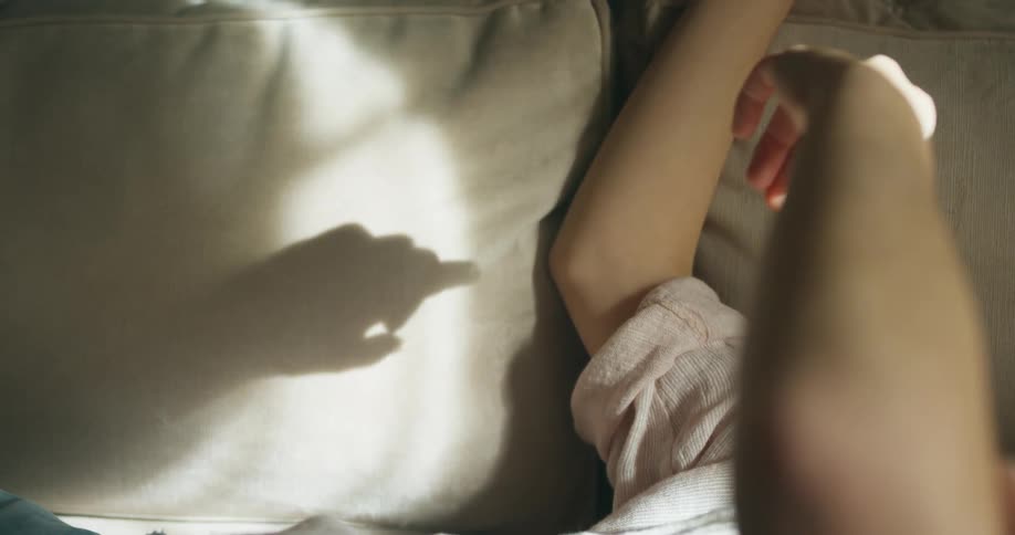 A person lies in bed and moves their hand to create shadow on their pillow
