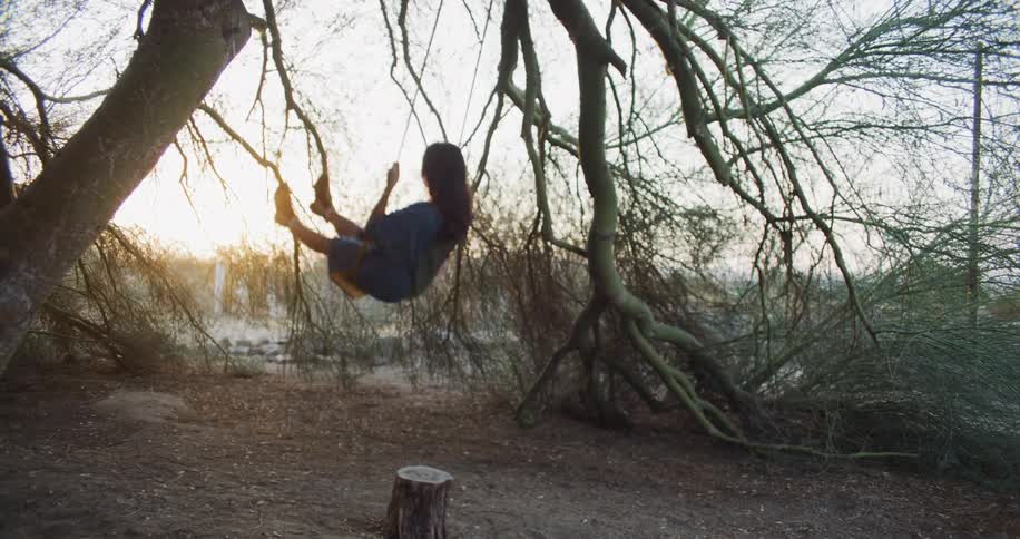 Woman wearing blue clothing on a tree swing in a forest area at sunset
