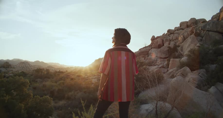 A woman stands at the bottom of a rocky hill and holds a stick as she looks around