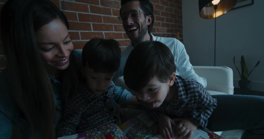 Father mother and the children sitting on the couch reading a childrens book together laughing and having fun