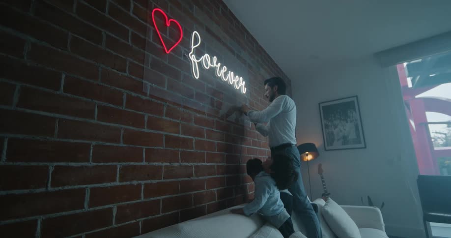 Father standing in the couch turning on a neon sign while his two boys are watching it excited