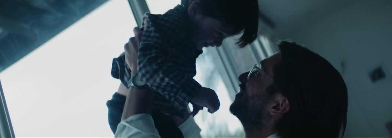 Father holding and lifting up his son in the air next to a big glass window indoors