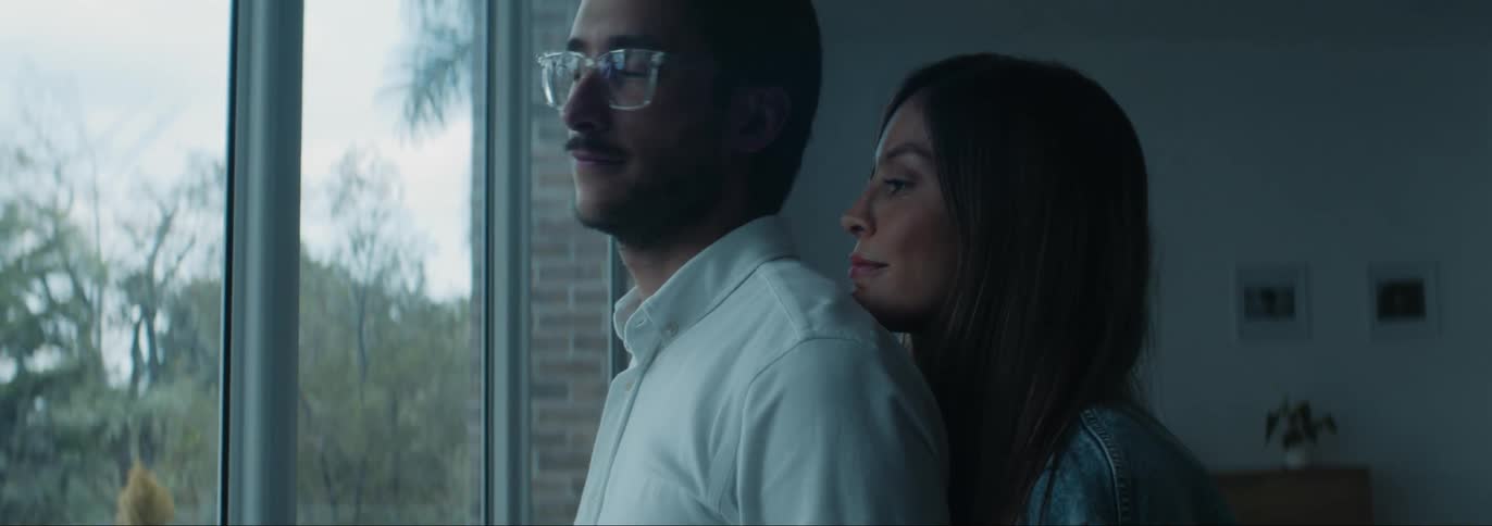 Woman hugging her husband from behind while they look ahead through the glass window