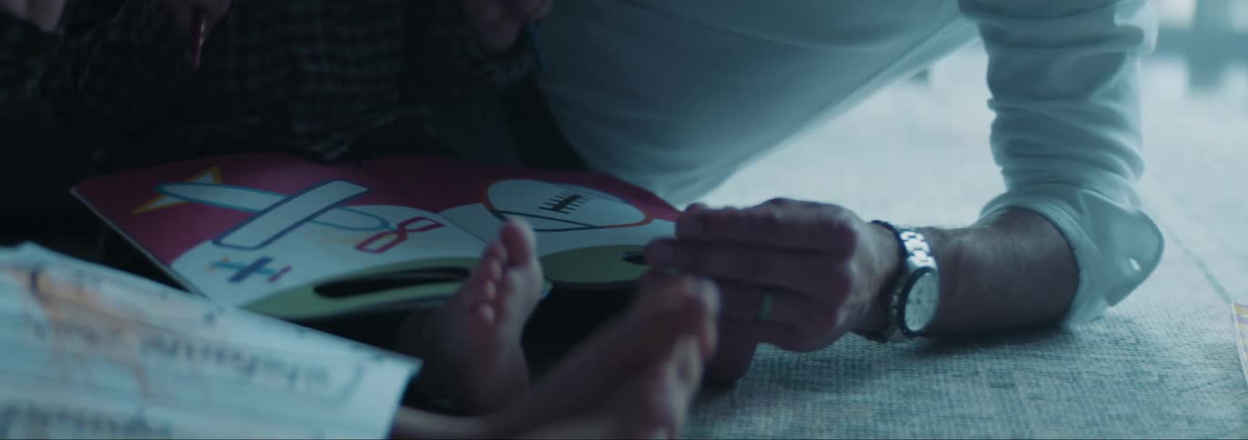 Father sitting down in the floor with his two sons and helping them with their coloring book and reading book at the living room