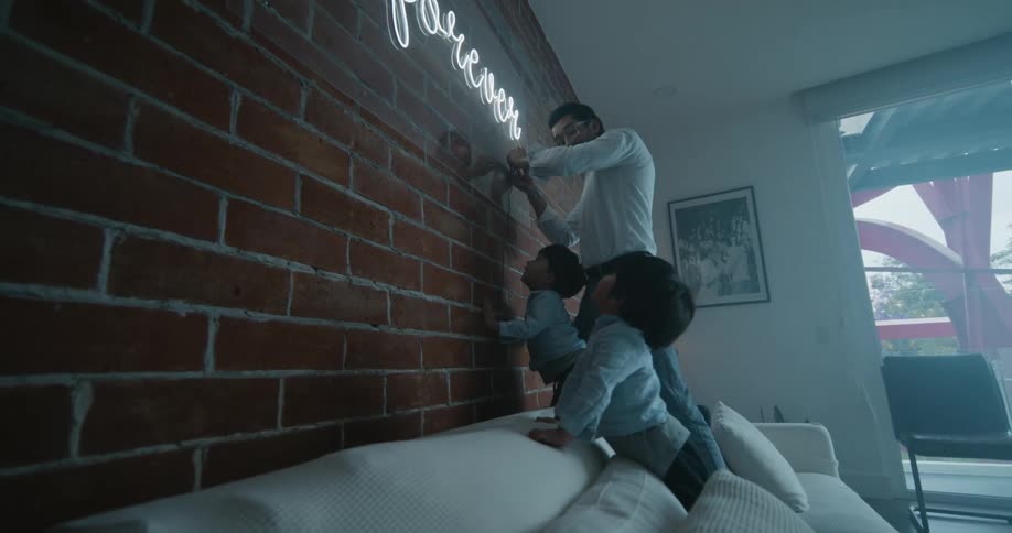 Father standing in the couch and turning on the neon lights at the wall while his children watch in awe