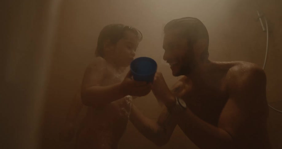 A smiling father helps wash one of his two children that are in the shower with him