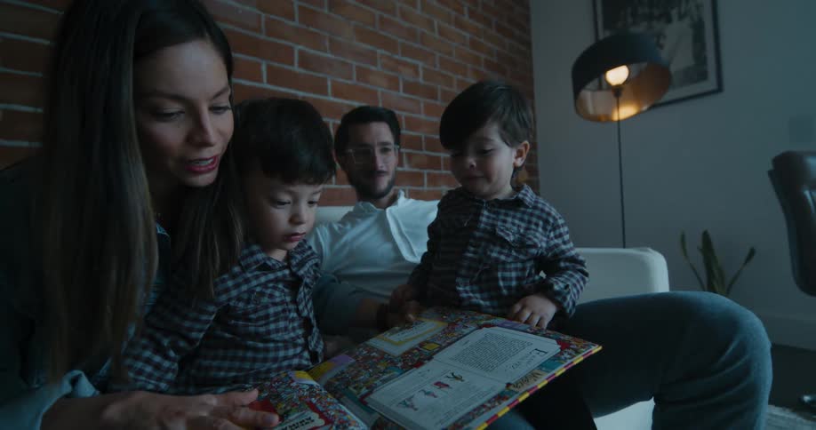 Mother father and the children sitting in the couch reading a childrens book together