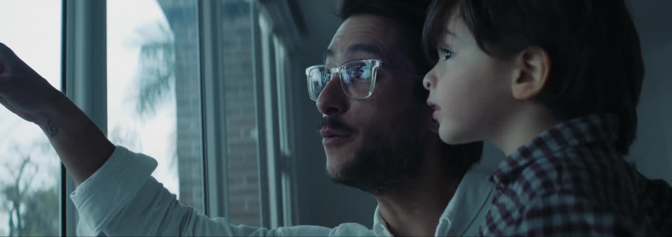 Father with glasses beard and white shirt holds son looking out the windows