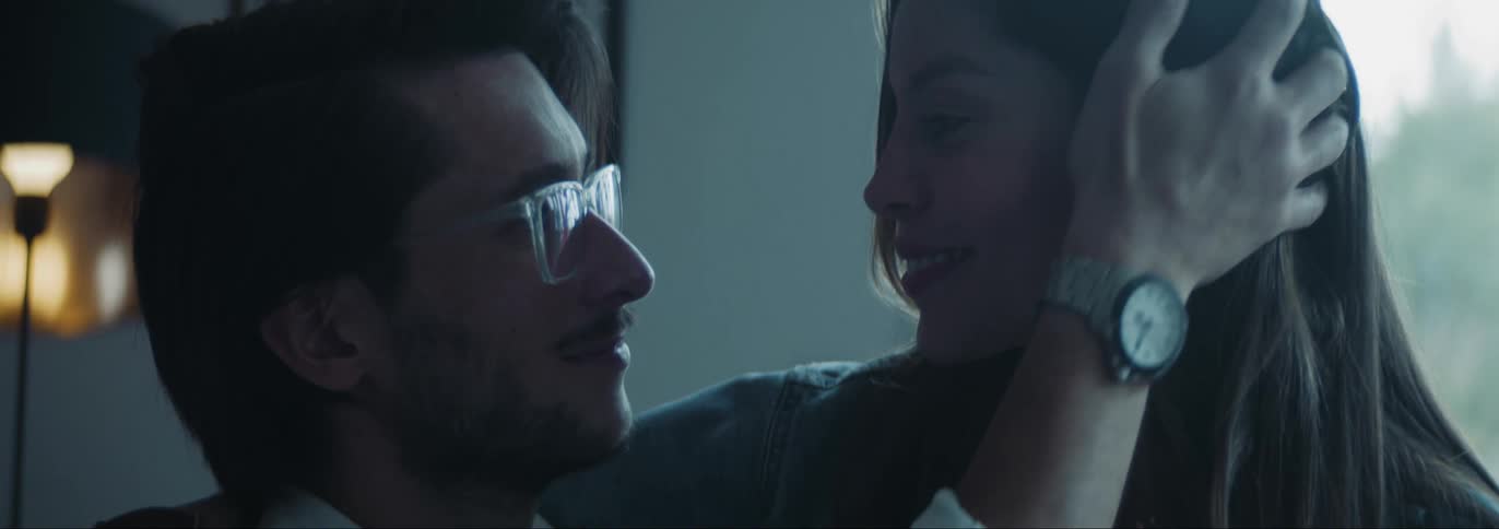 Man with glasses and beards lovingly look into womans eyes and touches her hair