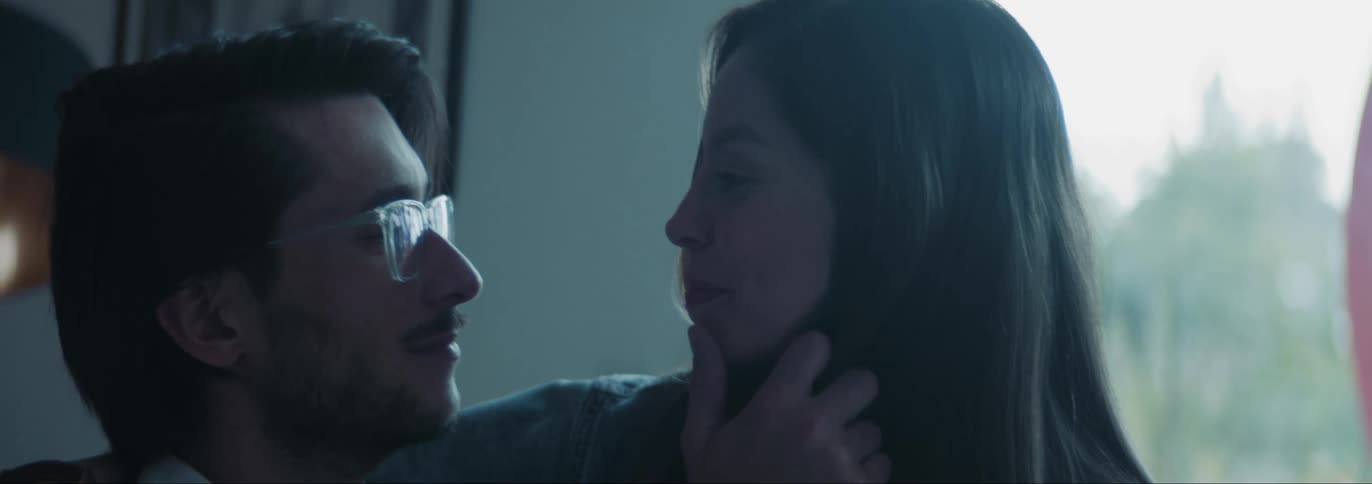 Man gently touching the hairs and face and romantically looking at a woman sitting in his lap indoors