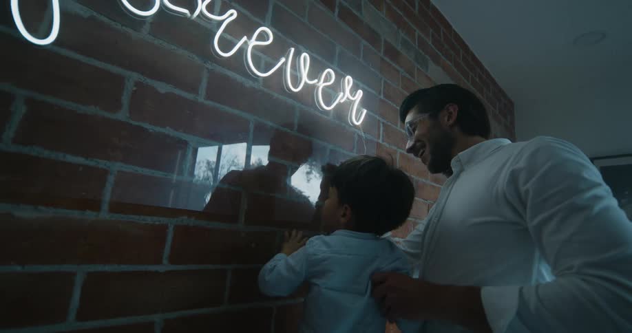 Father and son turning on the neon sign at the wall inside of the house