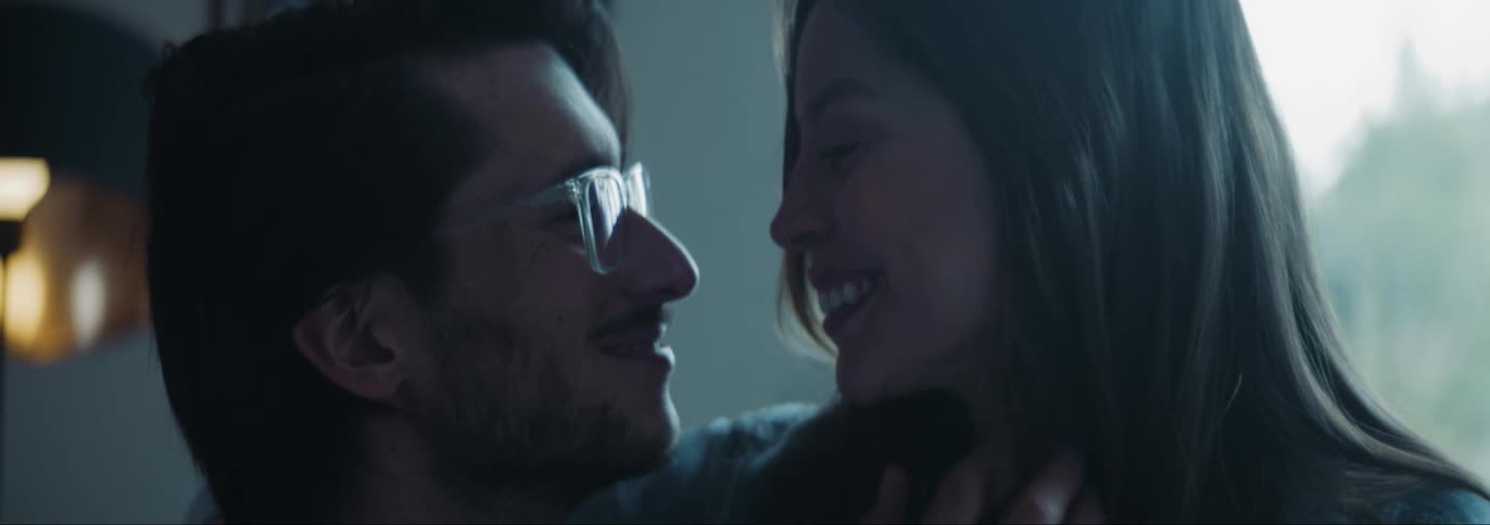 Man with beard and glasses lovingly looks into womans eyes and touches her hair