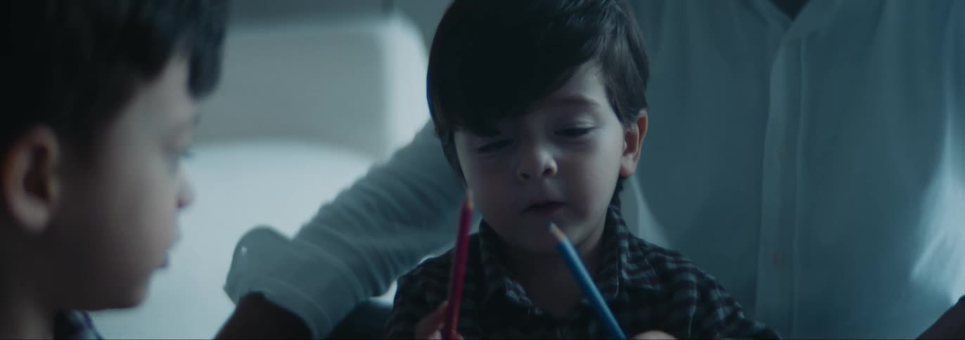 Man and boy watch a second boy play with colored pencils