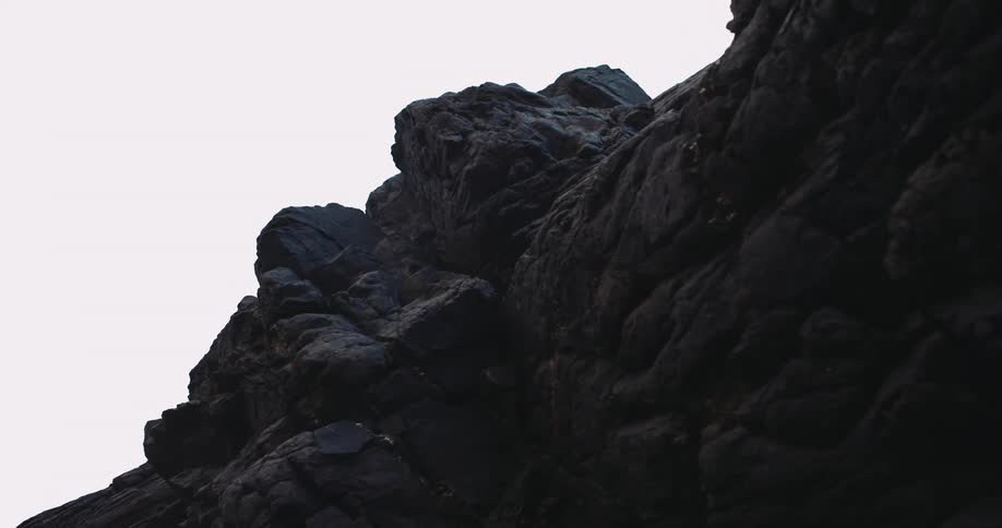 Light precipitationfalls past dark black craggy cliff side