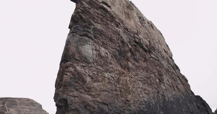 Narrow stone outcropping stands on rough rocky terrain with another stone mound in the background