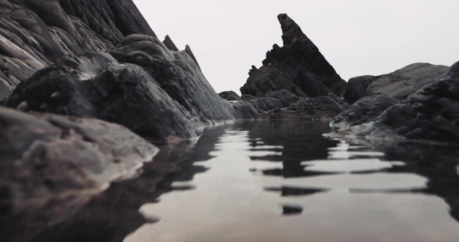 Water reflects the images of rocks surrounding the water and moving as the water ripples