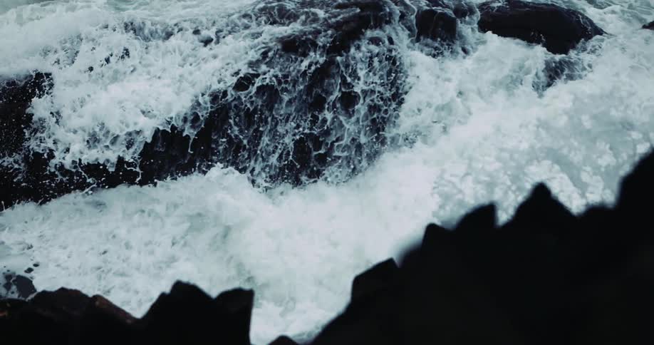 The ocean waves crash into the large rocks and splash water over them