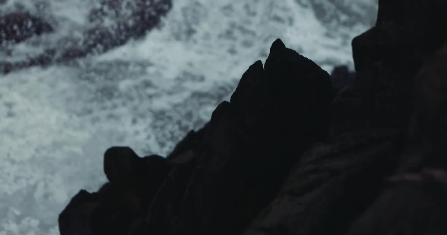 Rough water waves crash against rocks along the coast and roll over them
