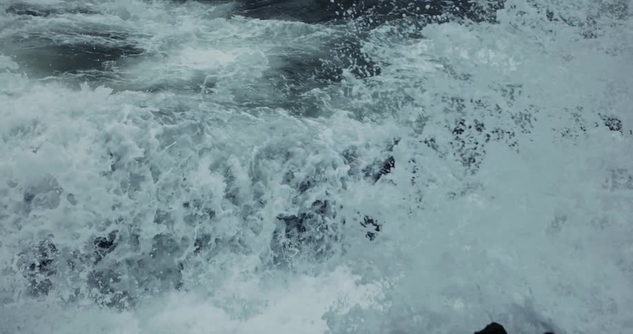 Rough water waves splash and crash against rocks along the coast and roll over them