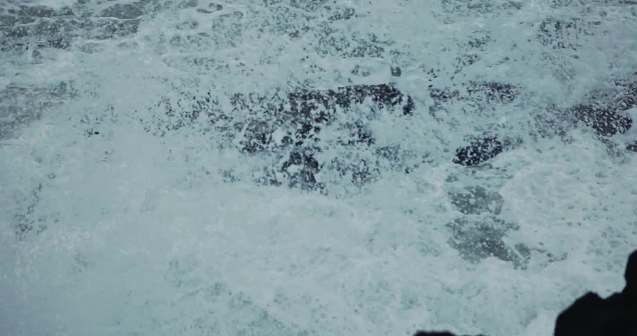 Rough water waves crash and splash against rocks along the coast and roll over them